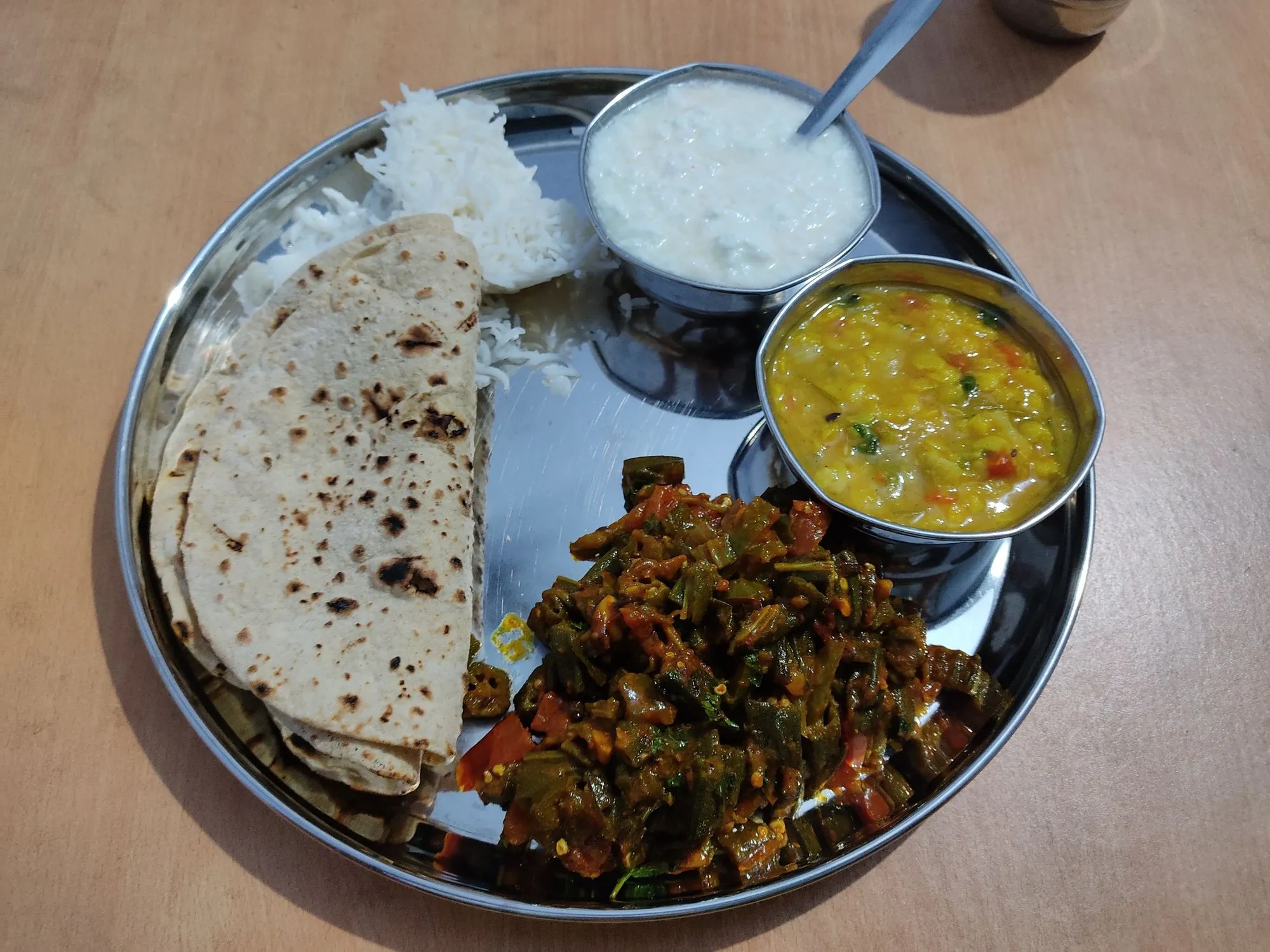 A steel plate with rotis, rice, bhindi sabzi, a bowl of yellow dal and a bowl of curd